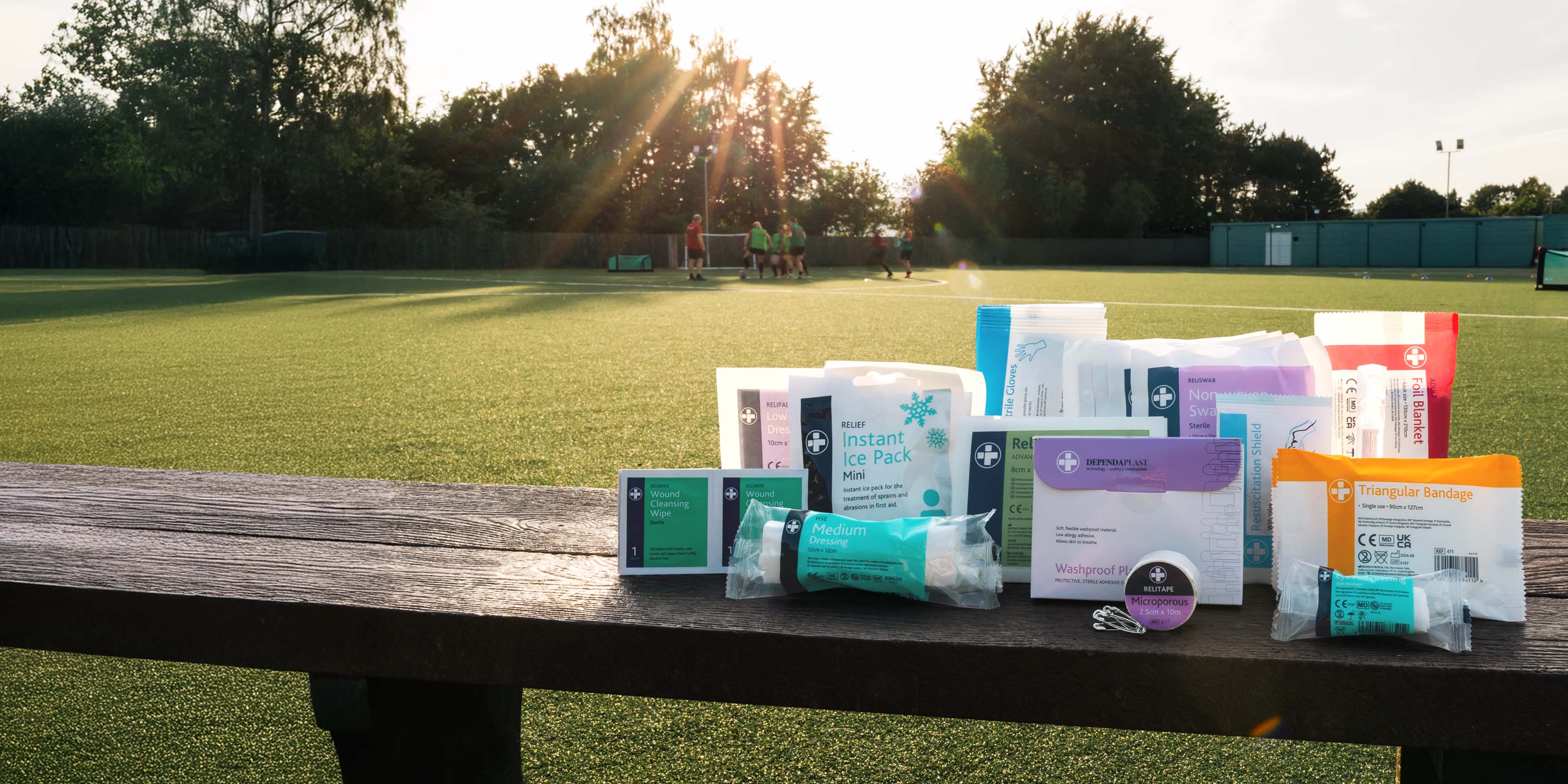 Assorted medical supplies on a wooden bench with a sports field background