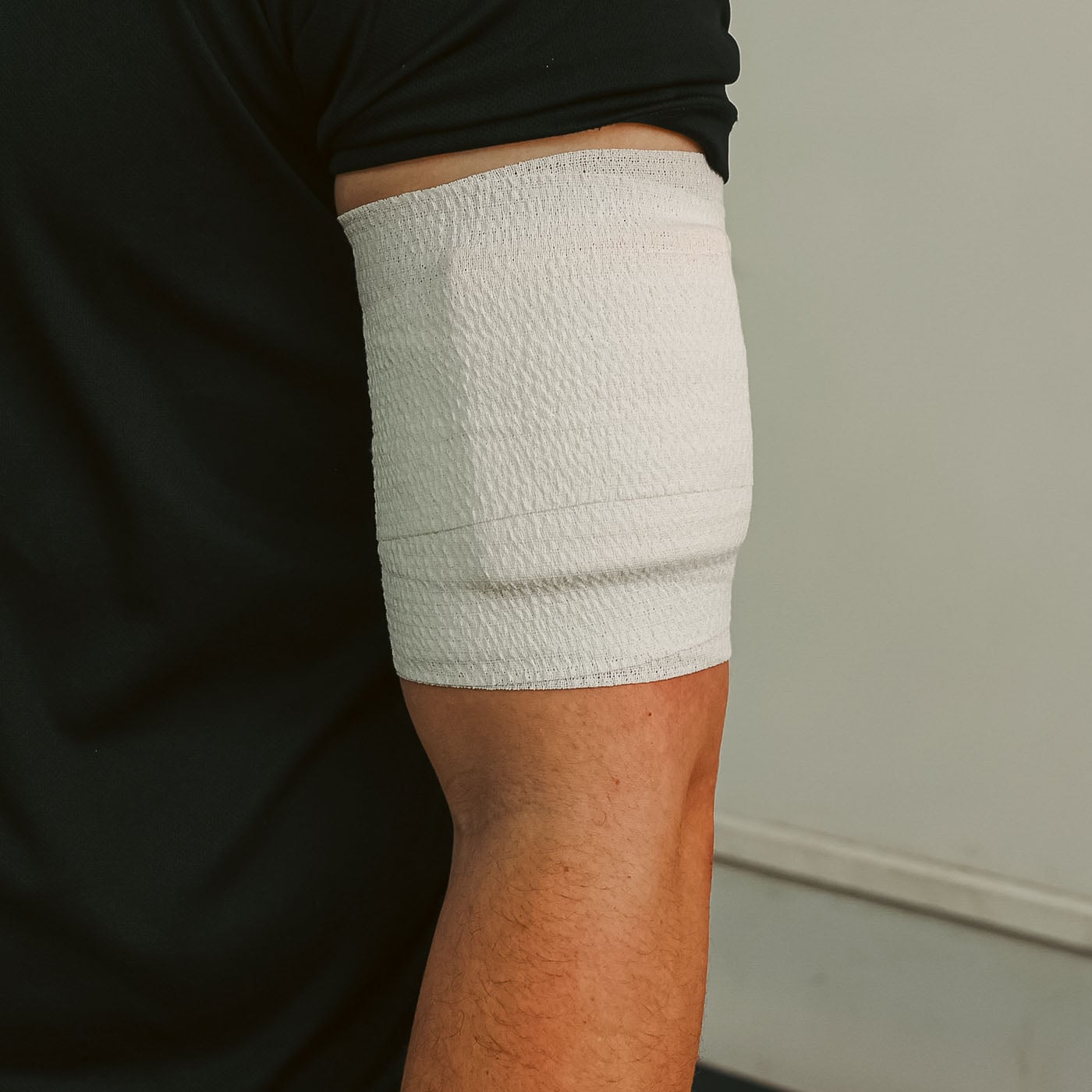 Person wearing a white bandage on their arm against a neutral background