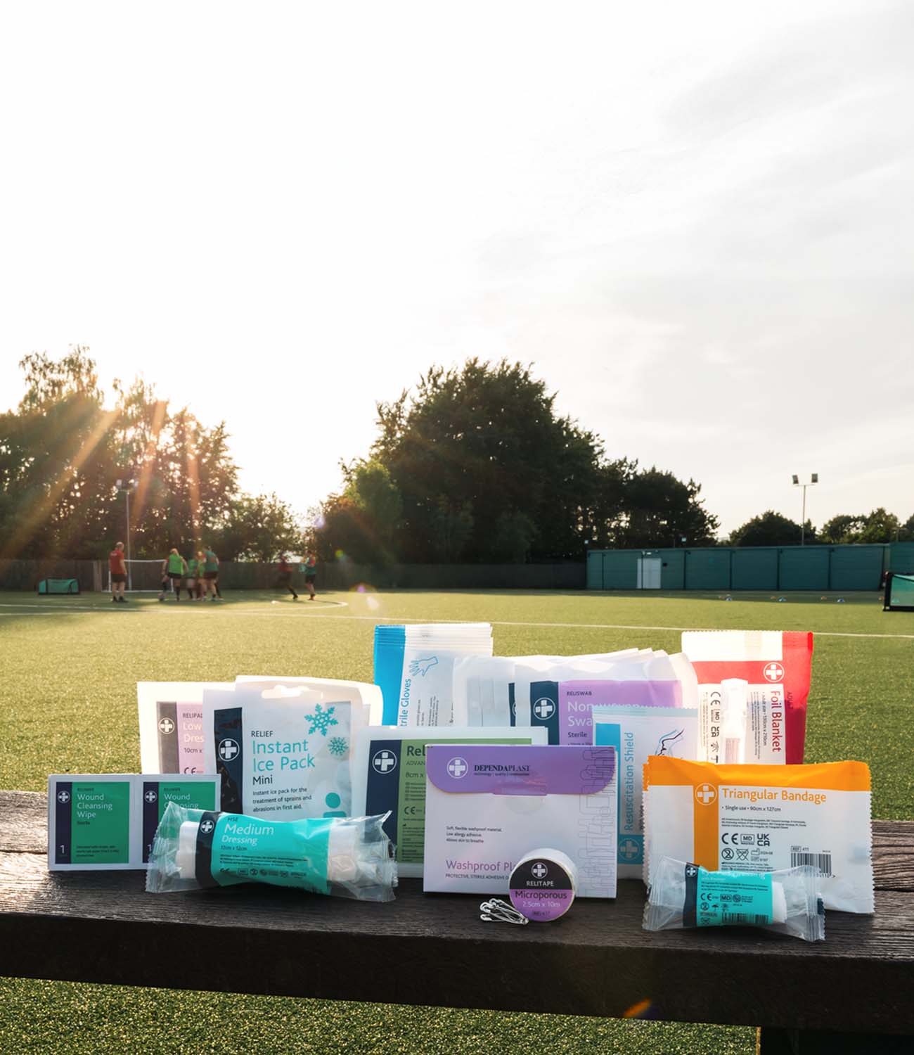 Collection of first aid kits on a wooden bench with a sports field background