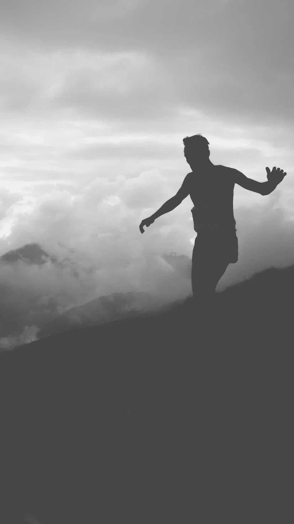 Silhouette of a person standing on a mountain with clouds in the background