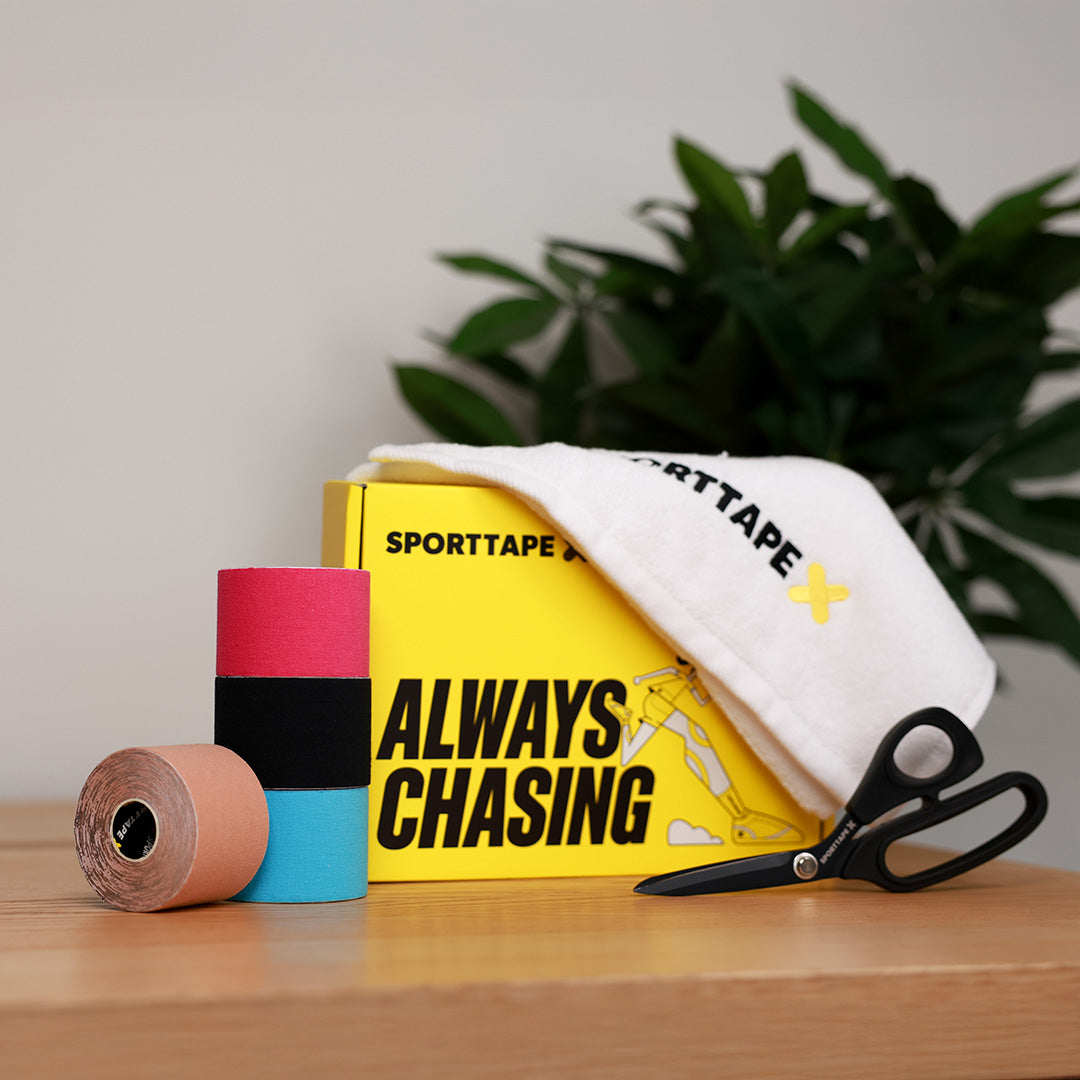 Sporttape with a box labeled 'Always Chasing' and scissors on a wooden surface.