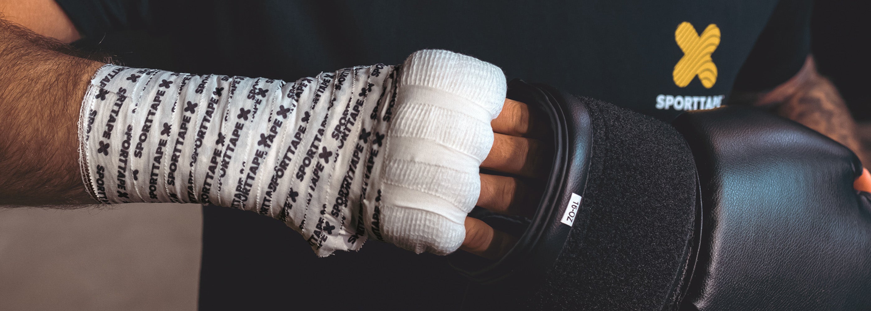 Athlete with Boxing hand wrap of Gauze and Zinc Oxide Branded 2.5cm, putting hand into a boxing glove.