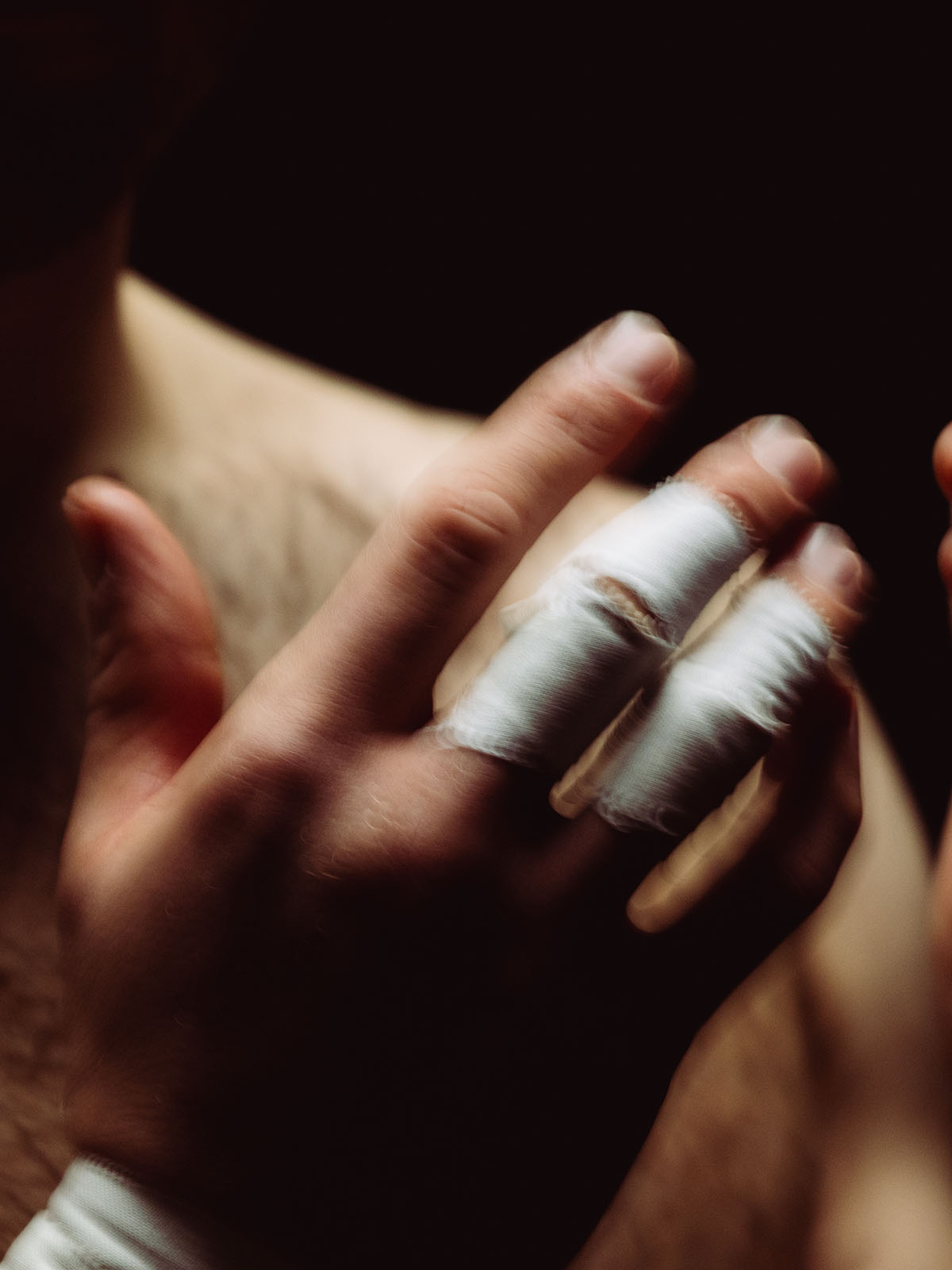 Close-up of hands with zinc oxide white tape on their fingers against a dark background