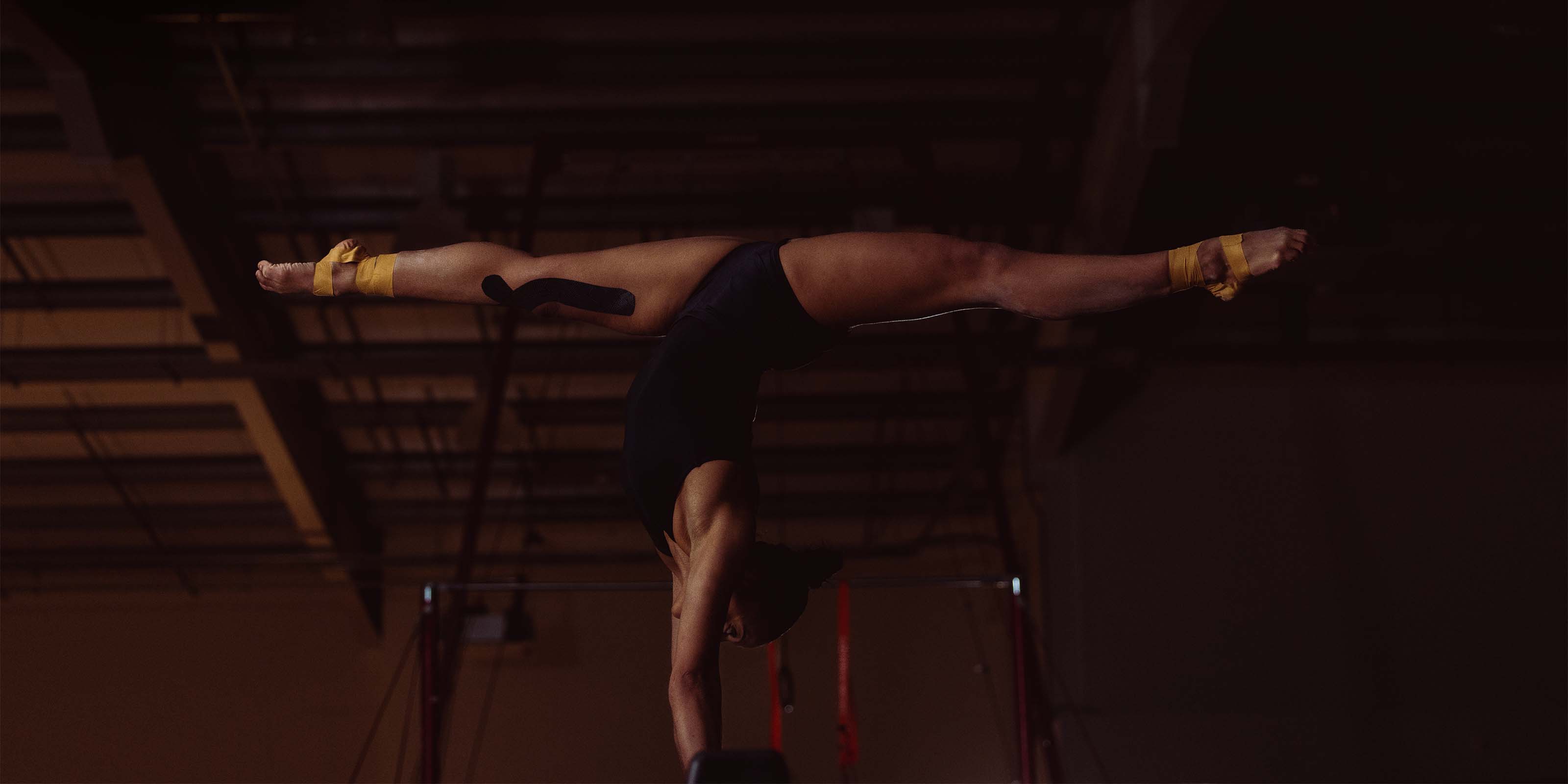 Person performing a handstand on a red mat in a dimly lit room.