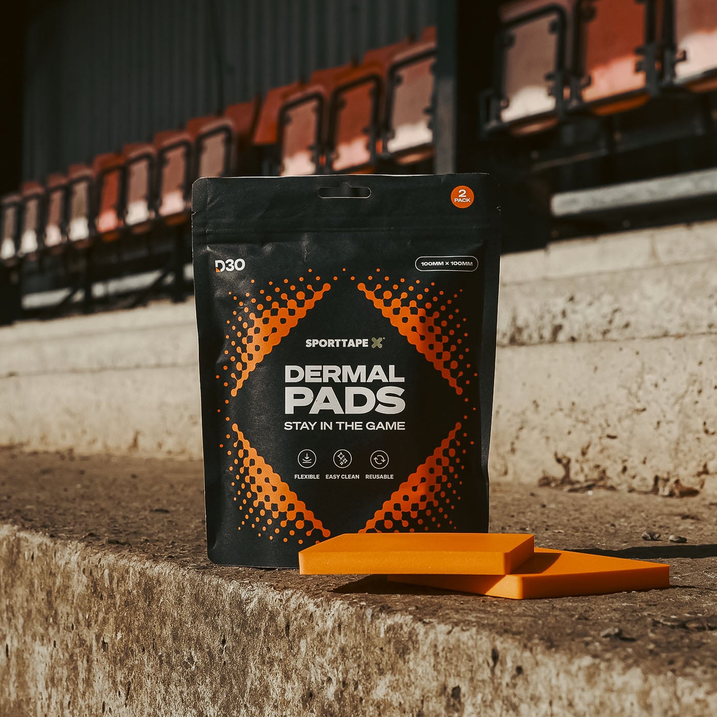 Sportape Dermal Pads packaging on a concrete surface with stadium seats in the background