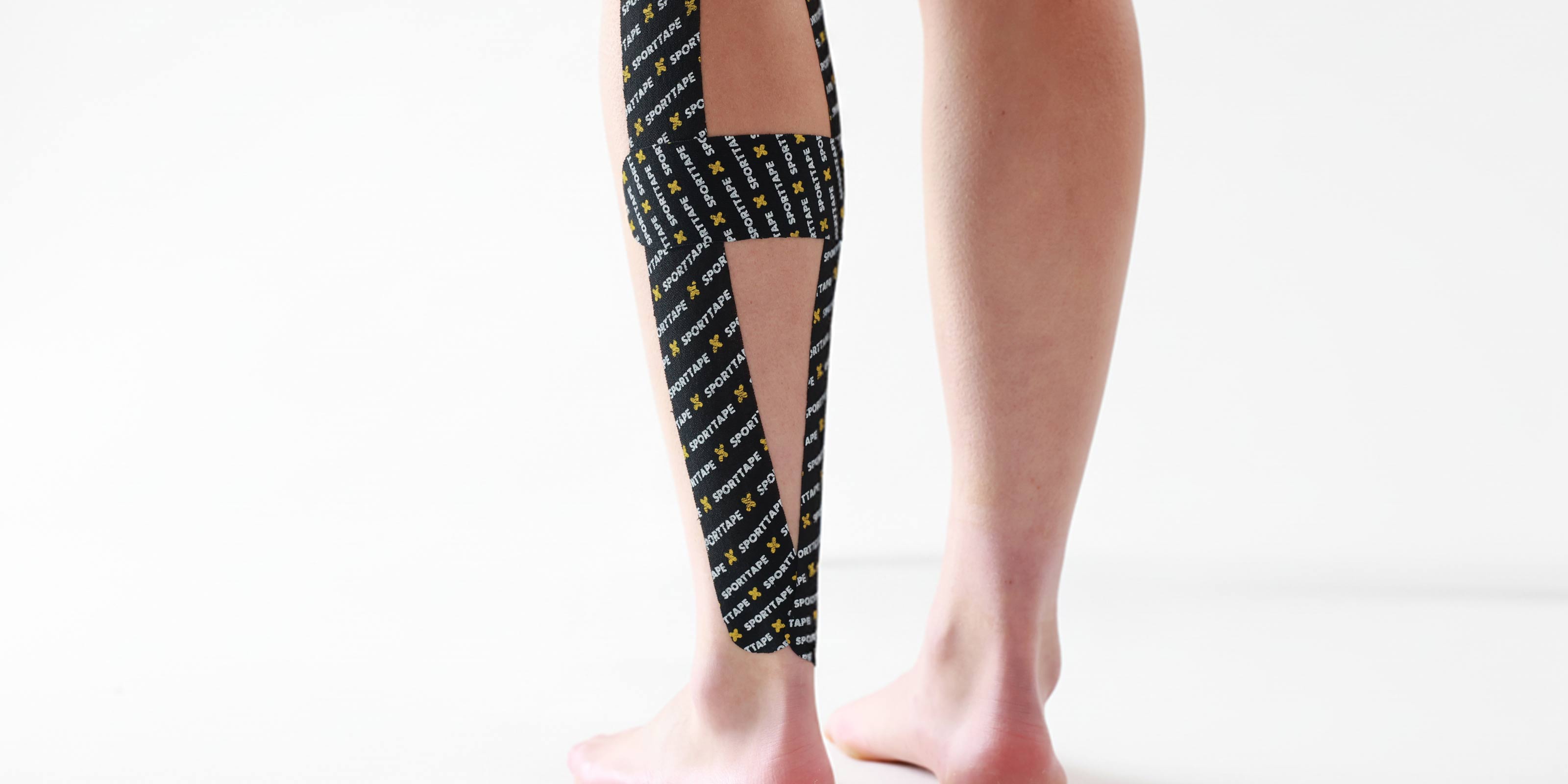 Person wearing a black and yellow Kinesiology tape on calf a white background