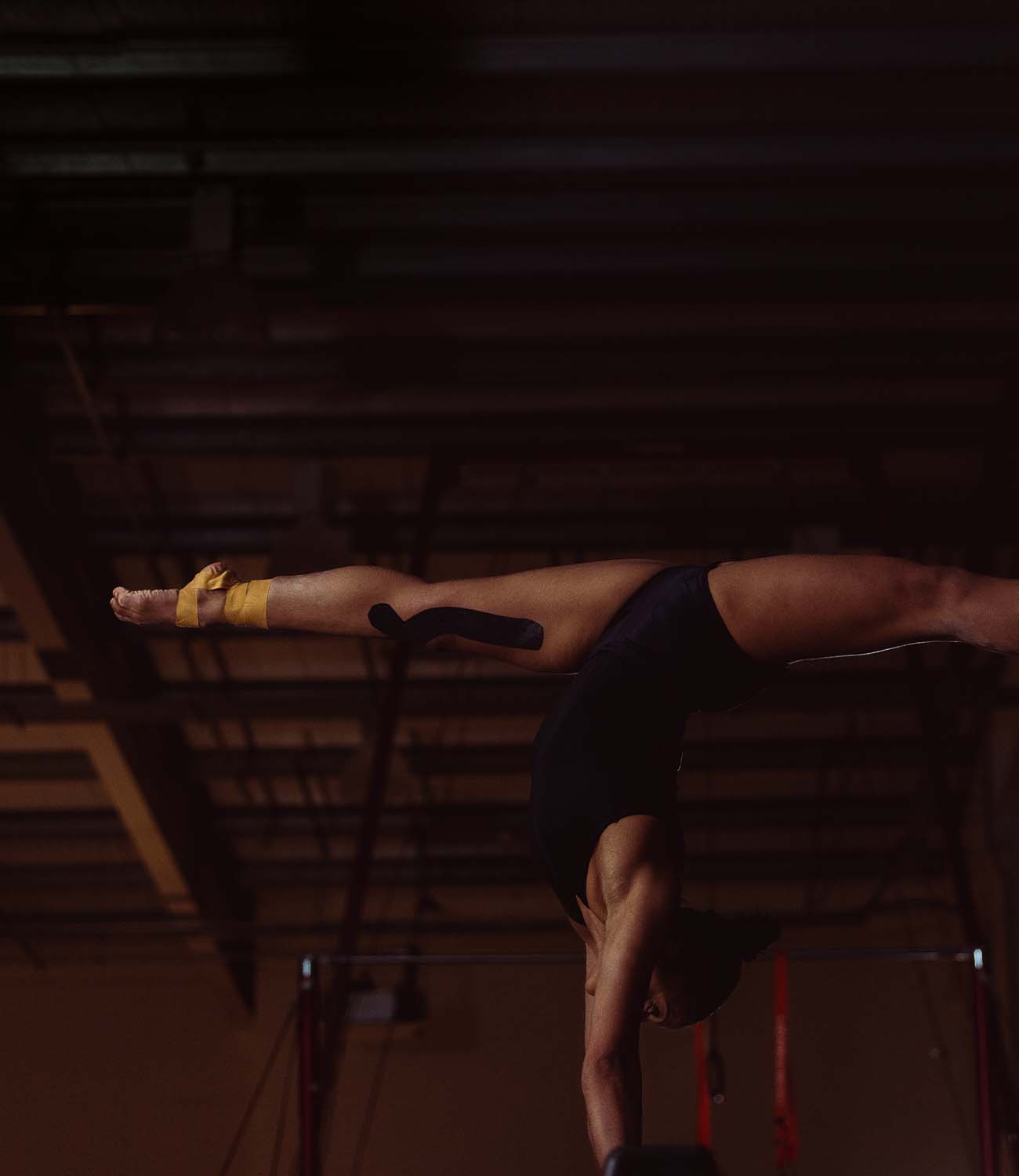 Person performing a handstand on a horizontal bar in a gym setting